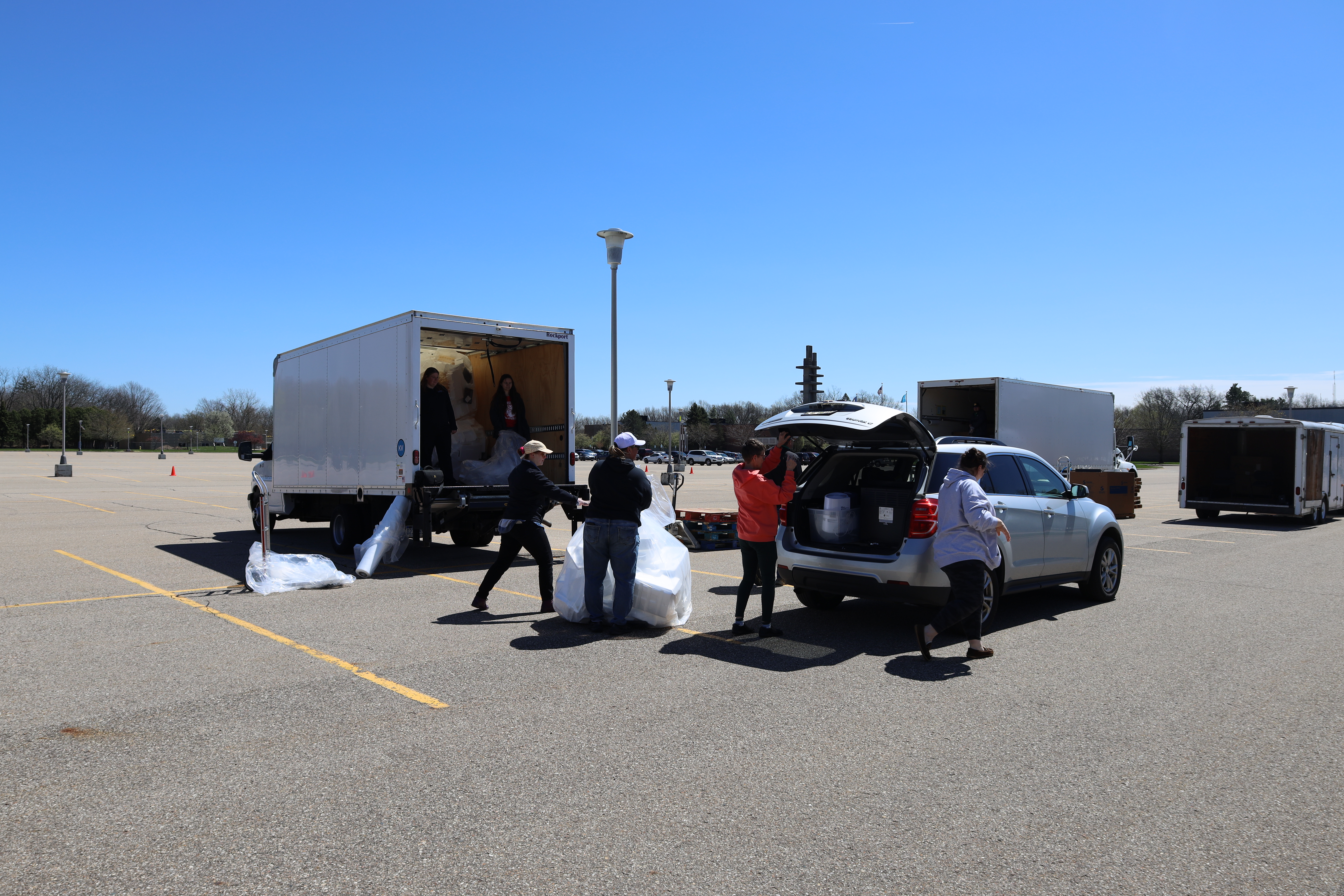 A wider shot of two vehicles, both with the back open, as people transfer objects from one to the other.